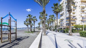 A beachfront promenade with palm trees, a playground, and a high-rise building in the background. - A&N Algarrobo Beach 5 (Algarrobo Costa)