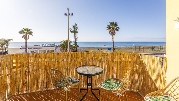 A balcony with a view of the beach, featuring a table and two chairs.