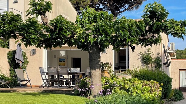 Ein Haus mit einer Terrasse, ausgestattet mit Tisch und Stühlen, umgeben von üppiger Vegetation und blühenden Pflanzen.