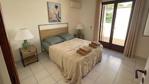 Ein ordentlich eingerichtetes Schlafzimmer mit einem Bett, zwei Nachttischen, einer Wand-Klimaanlage und einer Tür, die auf einen Balkon führt.