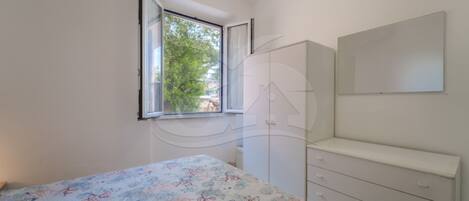 Een slaapkamer met een bed, een dressoir, een spiegel en een raam met uitzicht op bomen.