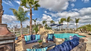A poolside area with wicker furniture, a stone fireplace, and a view of a swimming pool. - Book Your Stay at Casa da Saudade | Pool, Slide, & Wine Country Views (Temecula)