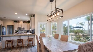 A modern kitchen with white cabinets, a wooden island, and a dining area with a large table and wicker chairs. - Book Your Stay at Casa da Saudade | Pool, Slide, & Wine Country Views (Temecula)
