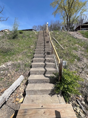 Steps lead up a hill, flanked by railings, through a natural setting with trees and shrubs.