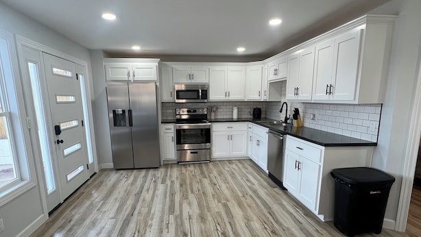 A modern kitchen with white cabinets, stainless steel appliances, and a wooden floor. - Peaceful Lakefront Cabin (Lincoln)