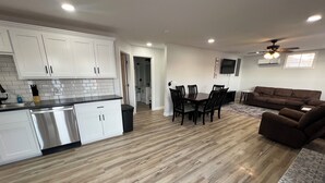 A modern kitchen with white cabinets and a dishwasher, a dining area with a wooden table and chairs, a brown sofa, and a ceiling fan. - Peaceful Lakefront Cabin (Lincoln)