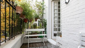 Un petit espace extérieur aménagé avec un banc et une table, entouré d’un mur en briques blanches et d’une clôture en métal noir.