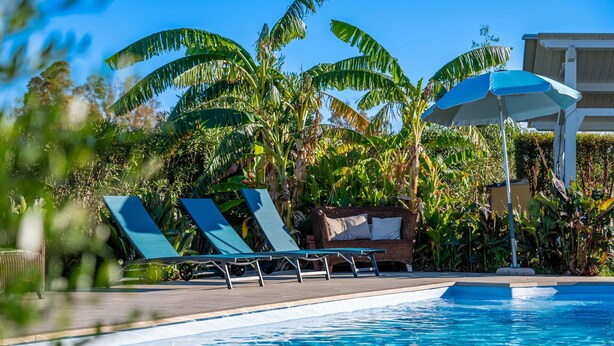 A poolside area with lounge chairs and umbrellas, surrounded by lush tropical vegetation. - House for 12 with Pool (Masone Pardu)
