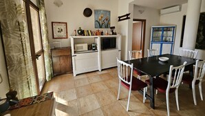 A compact kitchen with a microwave, stove, and white cabinets. There is a dining table with white chairs and a blue cabinet with glass doors. - House for 12 with Pool (Masone Pardu)
