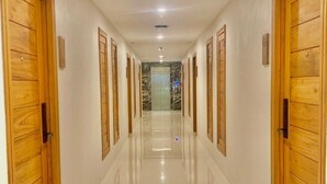 A long, well-lit hallway with wooden doors on both sides, leading to an elevator. - Ozone hotel khhanom (Khanom)