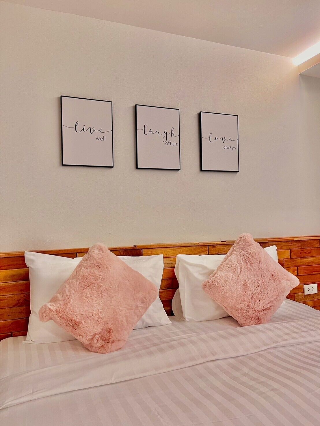 A bedroom with a wooden headboard, a bed with white and pink pillows, and three motivational posters on the wall.