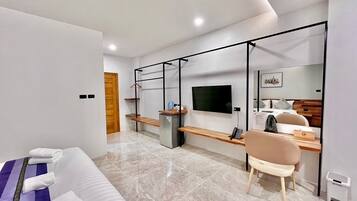 A modern hotel room with a sofa, a desk, a TV, and a mirror.