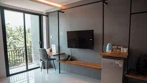 A modern hotel room with a large window, a flat-screen TV mounted on the wall, a wooden desk, a chair, and a small refrigerator. - Ozone hotel khhanom (Khanom)