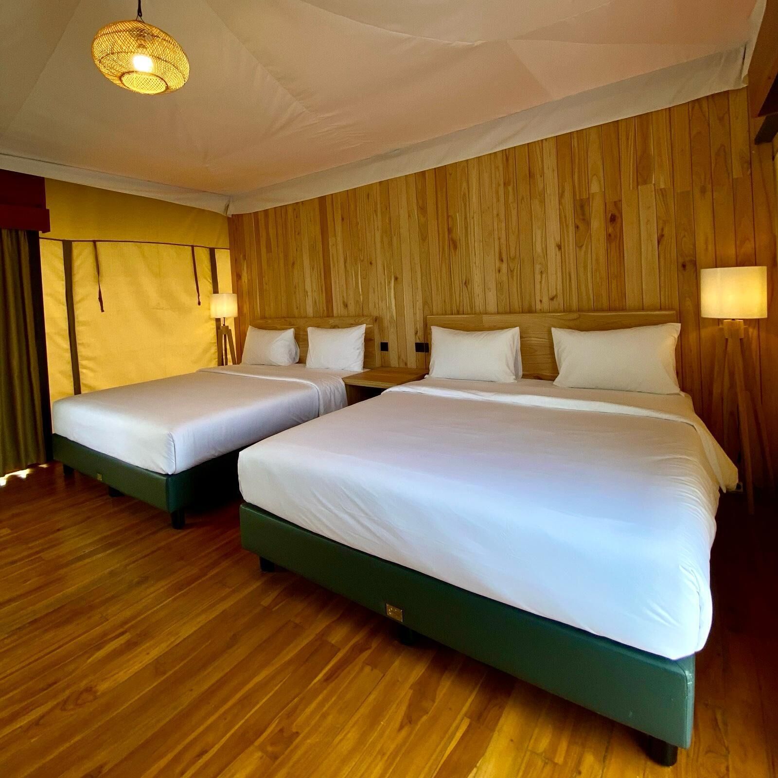 A hotel room with two beds, wooden panel walls, and a hanging light fixture.