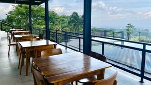 A covered outdoor dining area with wooden tables and chairs, overlooking a body of water and greenery. - Tebing View Glamping, Azana Hotel Collection (Parongpong)
