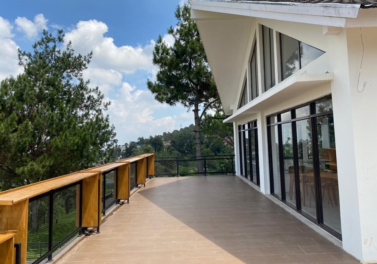 Un edificio moderno con terrazza in legno, ampie finestre e vista su alberi e colline.