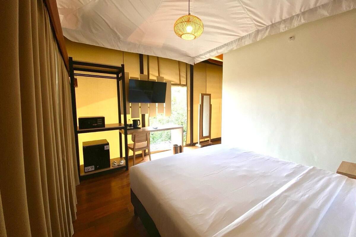 Une chambre d’hôtel avec un lit, un bureau et une chaise, une télévision et une grande fenêtre.
