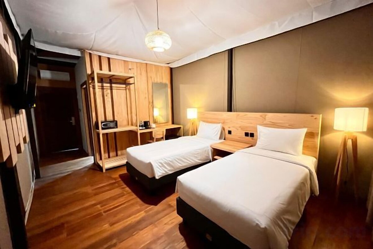 Habitación de hotel con dos camas, suelo de madera, televisor, lámparas de noche y armario.