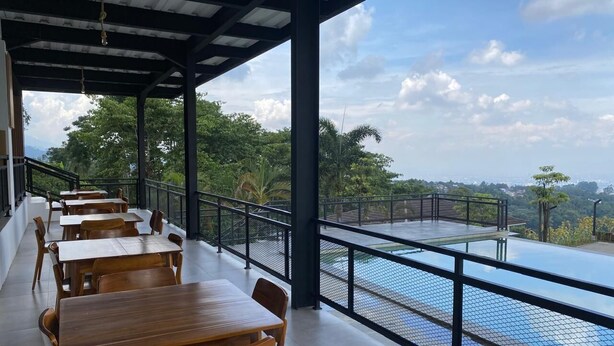 A covered outdoor seating area with tables and chairs, overlooking a swimming pool and lush greenery. - Tebing View Glamping, Azana Hotel Collection (Parongpong)