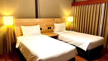 Una habitación de hotel con dos camas individuales, cabecero de madera, lámparas de noche y una cortina.