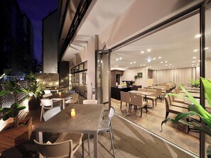 Un espace de restauration en plein air avec des tables et des chaises, un bar et une vue sur le paysage urbain la nuit.