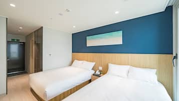 Habitación de hotel con dos camas, un cabecero de madera, un cuadro de una playa y una mesita de noche con un teléfono y una planta.