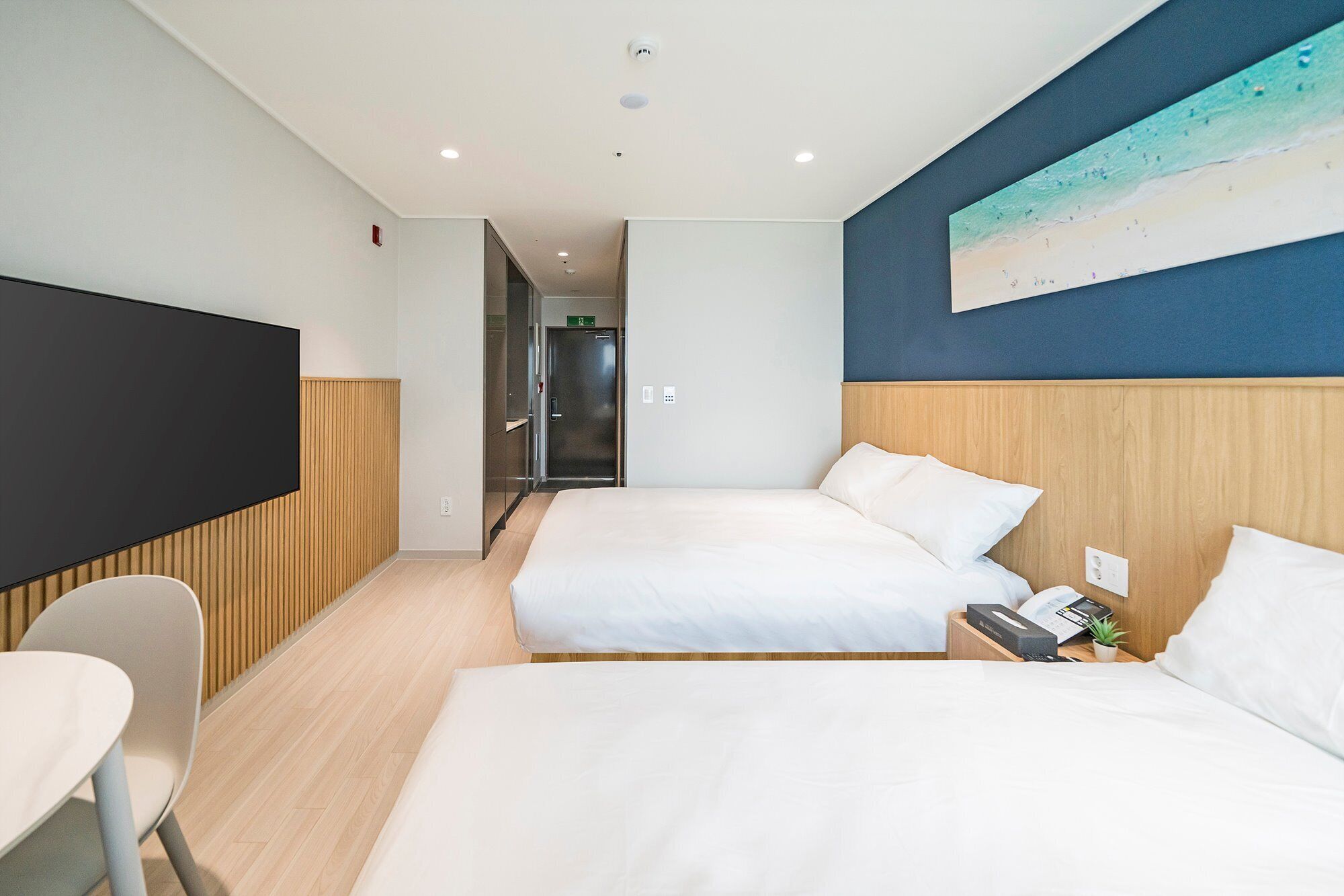 A hotel room with two beds, a flat-screen TV, a desk with a chair, and a painting on the wall.
