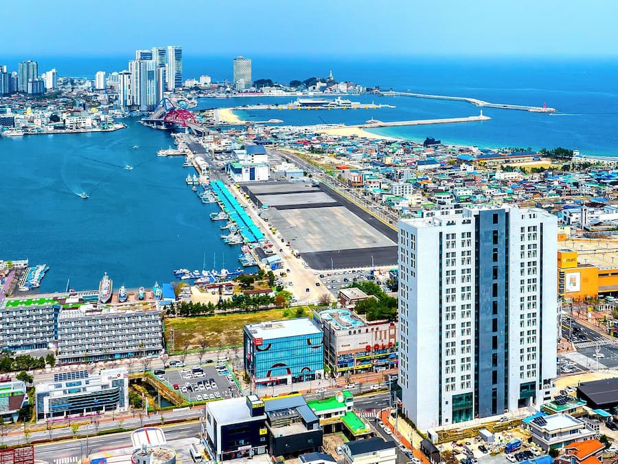 Paisagem costeira com marina, edifícios altos e uma praia.