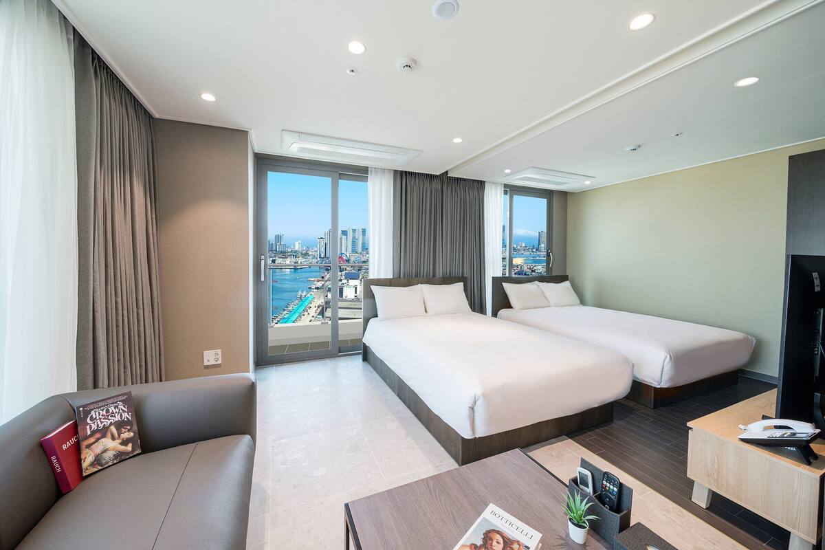 A hotel room with two beds, a sofa, a coffee table, and a TV.