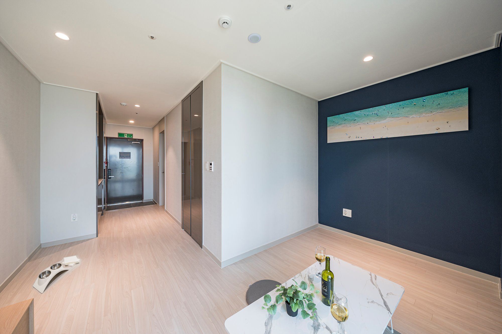 A modern interior with a dining area, a painting on the wall, and a hallway leading to an elevator.