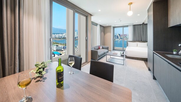 Habitación de hotel moderna con un balcón amplio, una zona de comedor con mesa y sillas, un sofá y una cama.