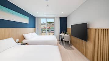 A hotel room with two beds, a TV, a small table with a chair, and a view of the outside.
