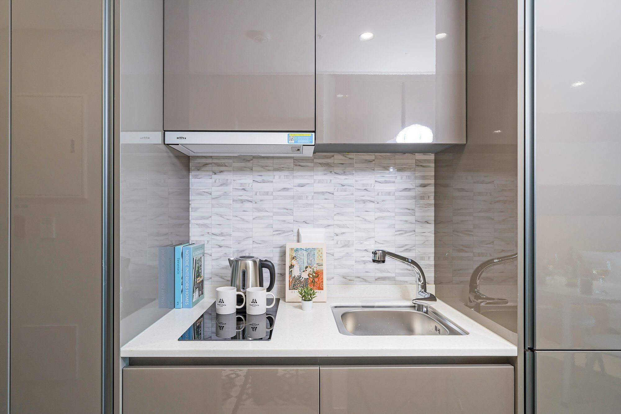 A modern kitchen with a stainless steel sink, a kettle, and two white mugs on the counter.