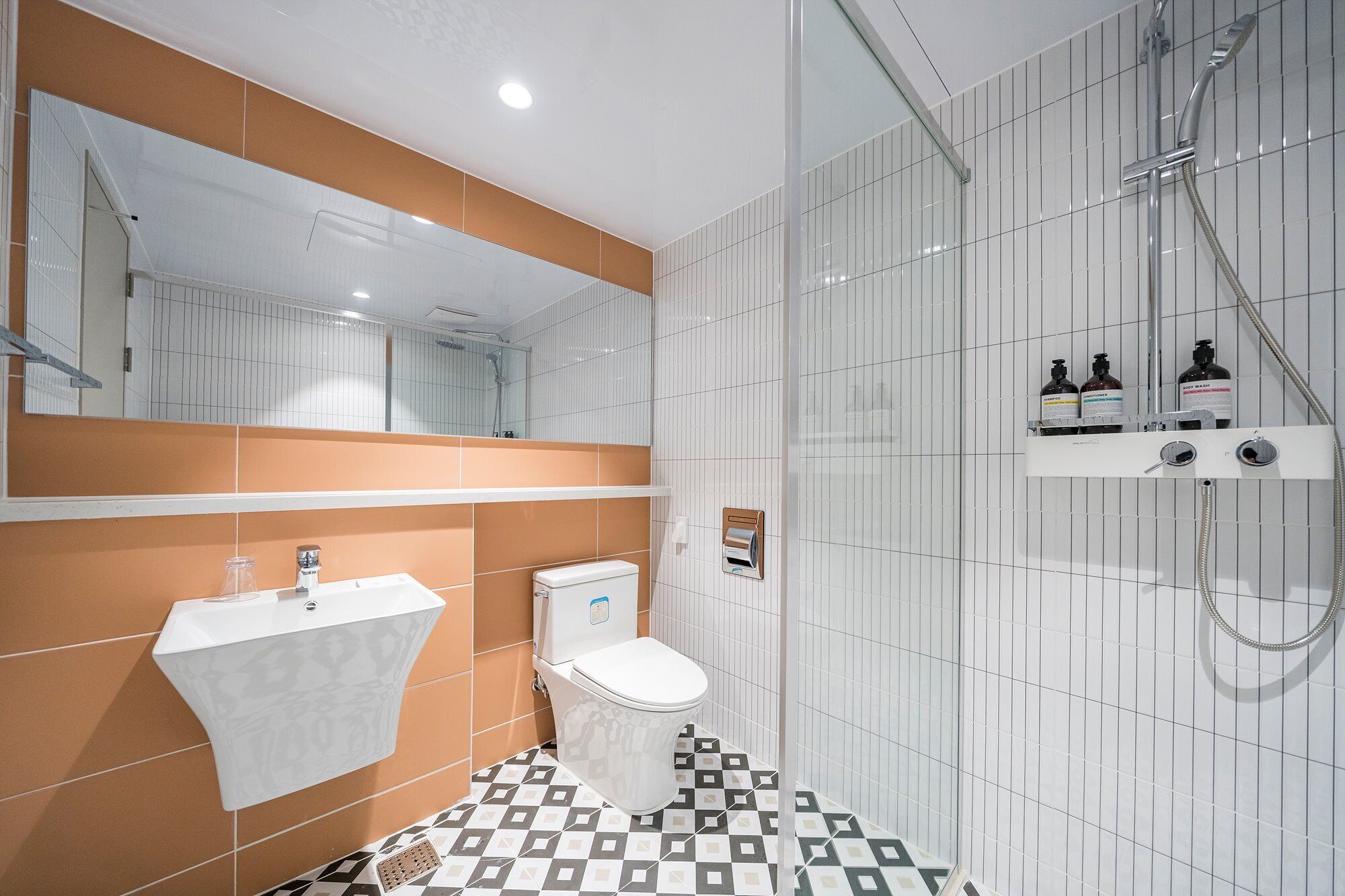 Un baño moderno con lavamanos, inodoro y ducha blancos. Hay artículos de aseo en la pared y un suelo estampado.