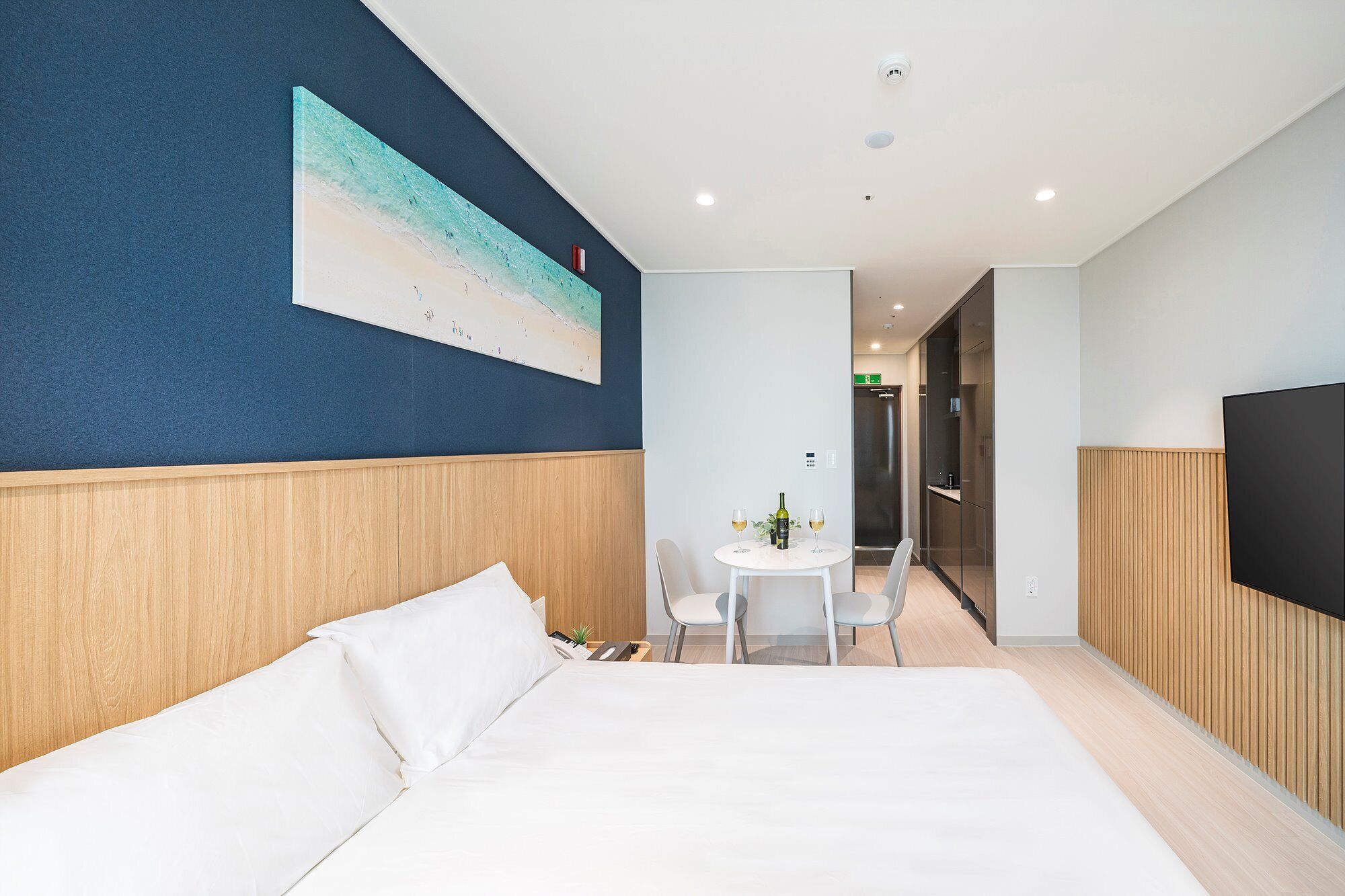 Habitación de hotel con una cama grande, una mesita con dos sillas, un cuadro en la pared y un televisor a la derecha.