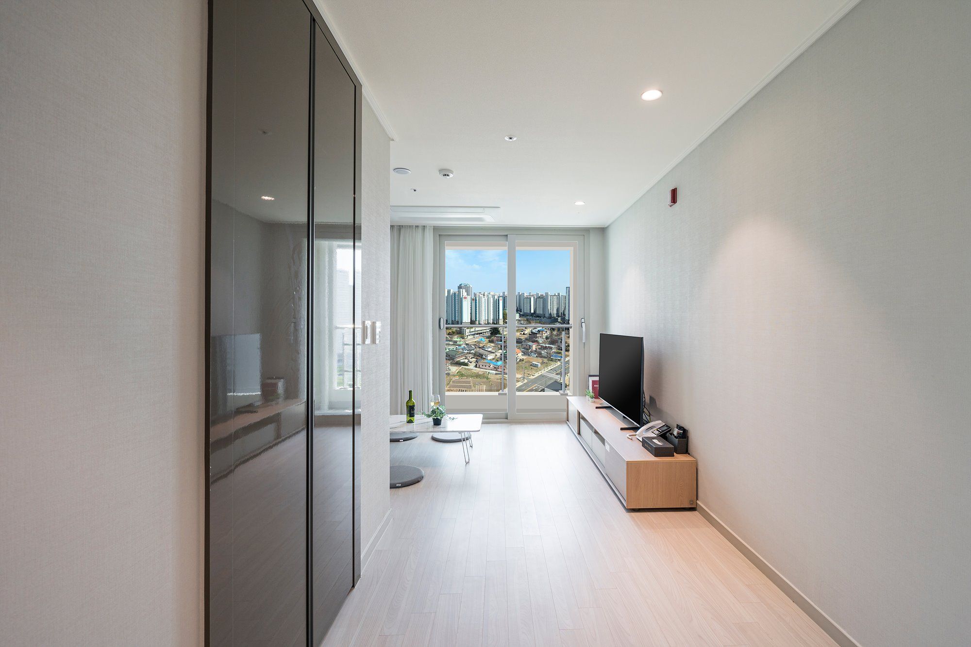 A modern apartment with a large sliding glass door leading to a balcony with a city view.