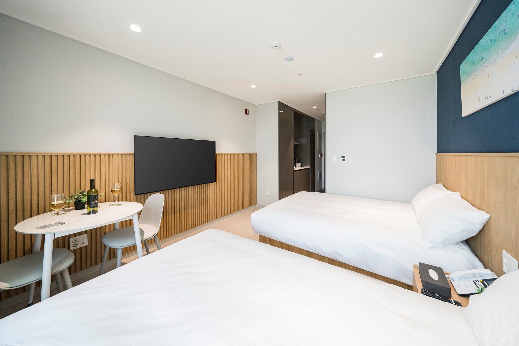 Een hotelkamer met twee bedden, een televisie, een klein tafeltje met een fles en glazen, en een stoel.