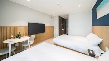 A hotel room with two beds, a TV, a small table with a bottle and glasses, and a chair.