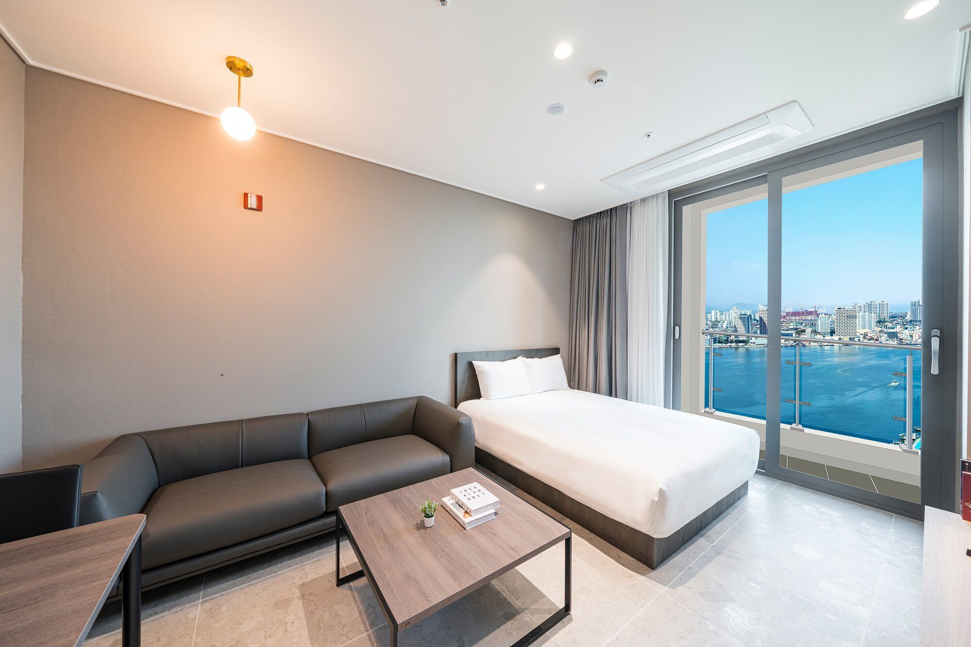 Une chambre d’hôtel moderne équipée d’un lit, d’un canapé, d’une table basse et d’une grande fenêtre donnant sur la ville.