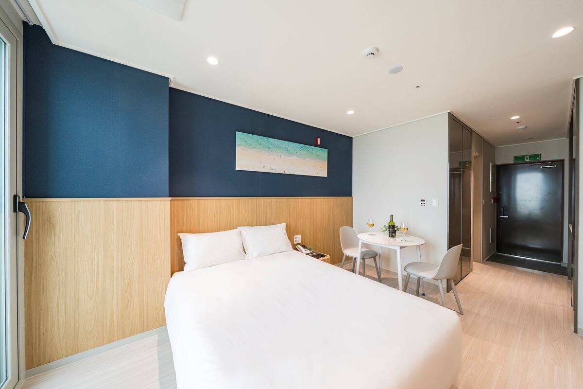 A hotel room with a bed, a small table with chairs, a painting on the wall, and a door leading to a bathroom.