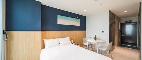A hotel room with a bed, a small table with chairs, a painting on the wall, and a door leading to a bathroom.
