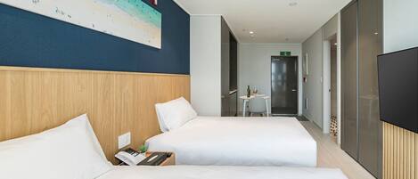 Ein Hotelzimmer mit zwei Betten, einem großen Gemälde vom Strand, einem kleinen Tisch mit Flasche und Glas sowie einem Fernseher an der Wand.