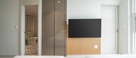 Una habitación de hotel moderna con una puerta corredera que da al baño, un televisor de pantalla plana montado en un panel de madera y dos camas con ropa blanca.