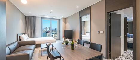 Una habitación de hotel moderna con cama, sofá, mesa de comedor con sillas, televisor y vista a la ciudad.