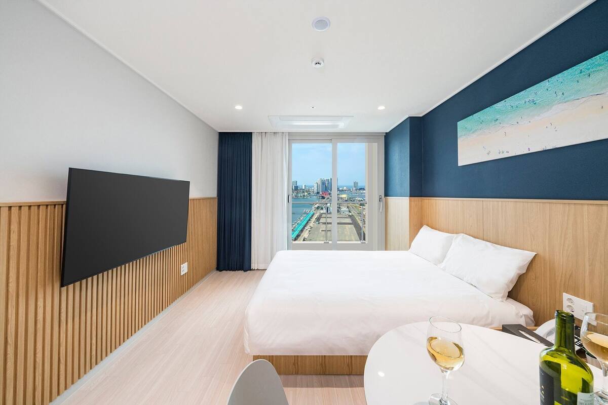 A hotel room with a bed, a TV, a glass of wine, and a view of the city.