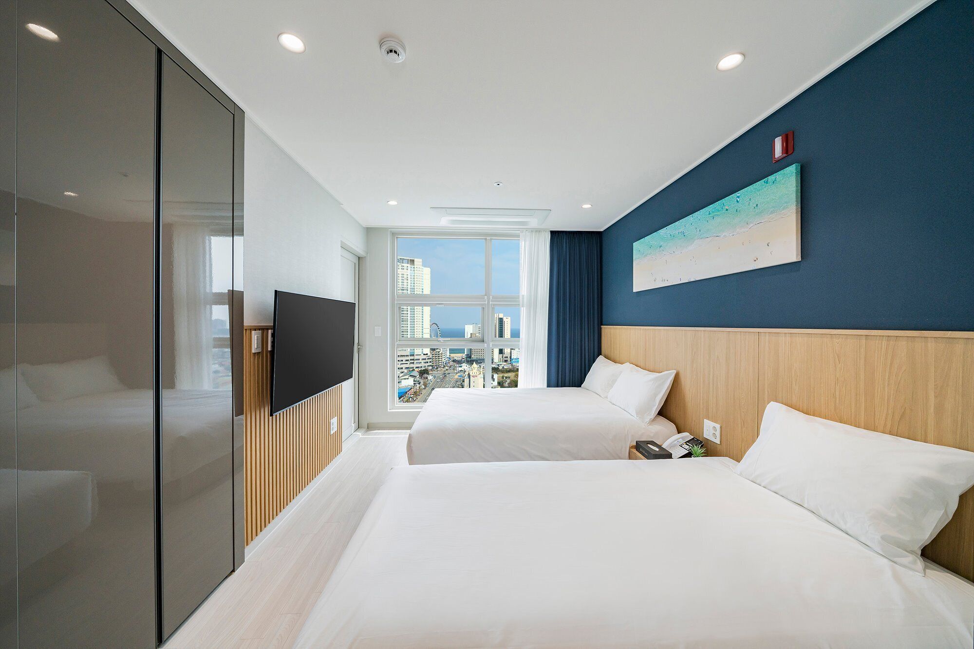 Habitación de hotel con dos camas, televisión, vista a la ciudad y un cuadro en la pared.