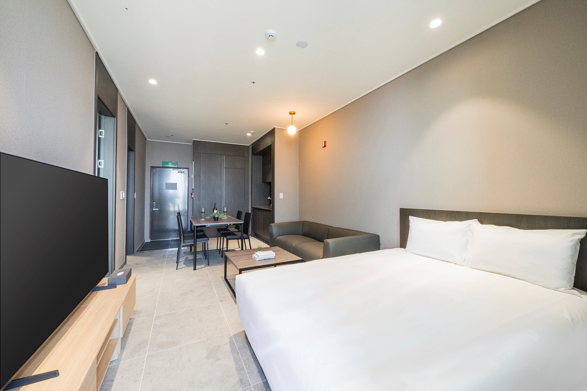 A modern hotel room with a large bed, a desk with a chair, a sofa, and a TV.