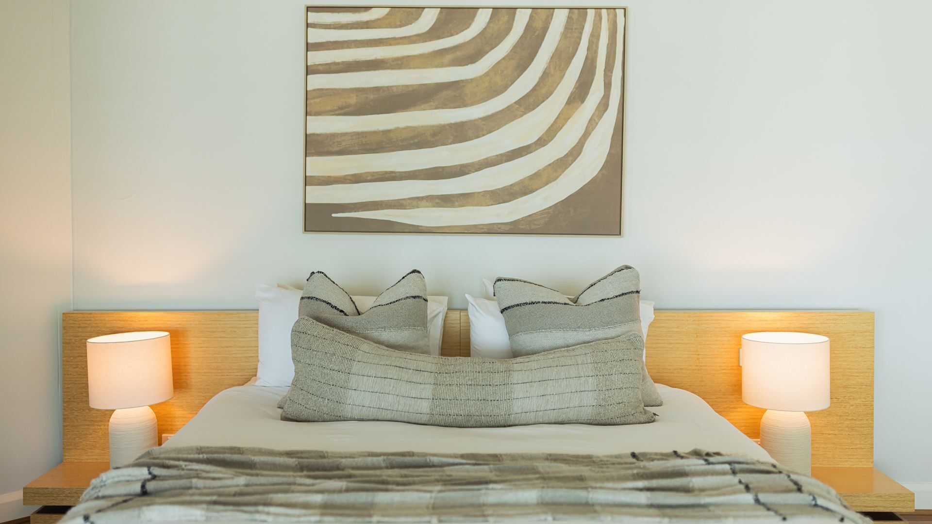 A neatly made bed with a striped blanket, two pillows, and two bedside lamps.