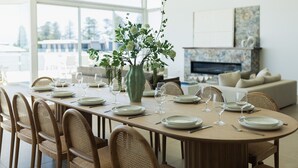 Un coin repas avec une longue table dressée pour le repas, entourée de chaises en osier, et un vase rempli de verdure placé au centre.