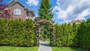 A pathway leading to a house with a brick facade and a rose archway.